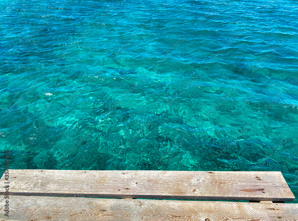 Wooden pier in the middle of transparent pristine turquoise sea water in Playa de Muro, Mallorca