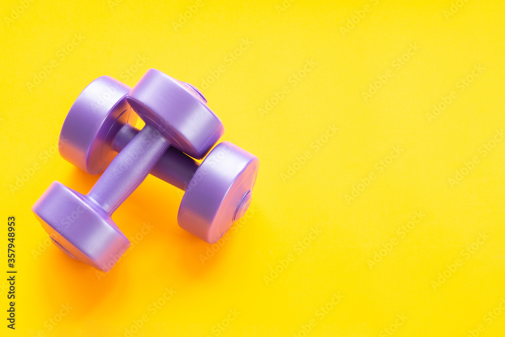 Two purple dumbbells, one lying on the other, on a yellow background Two purple dumbbells, one lying on the other, on a yellow background