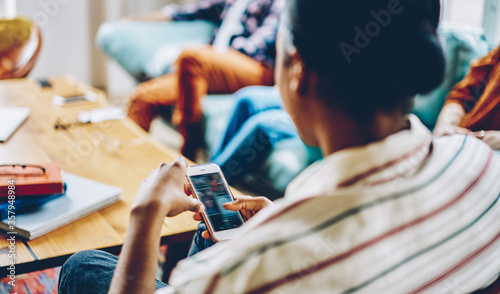 Crop African American woman surfing cellphone during meeting with friends