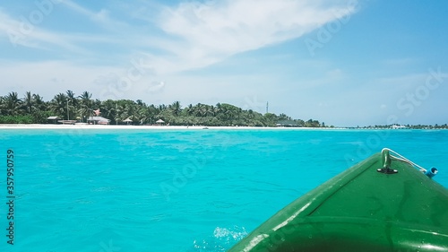Close up view of green canoe nose with tropical island in the background. Crystal clear tortoise water and blue sky on a sunny day. Relaxing water sport on isolated water far from land in Maldives.