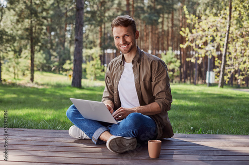 Charismatic smiling male sitting with a notebook outdoors