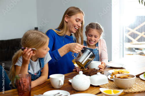 Cheerful mother drinking tea with adorable daughters at home