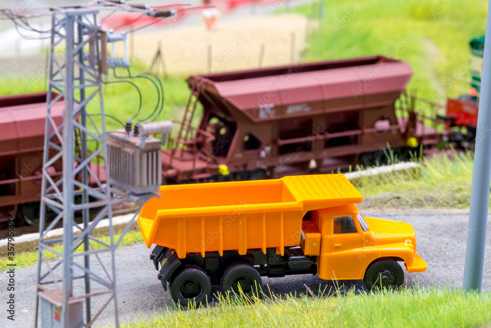 Orange truck on model train layout with moving freight train in behind Orange truck on model train layout with moving freight train in behind