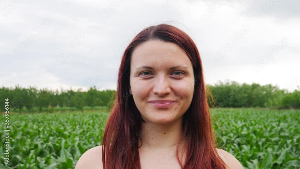 A portrait of a caucasian woman with red hair standing in a field smiling at the camera. A portrait of a caucasian woman with red hair standing in a field smiling at the camera.