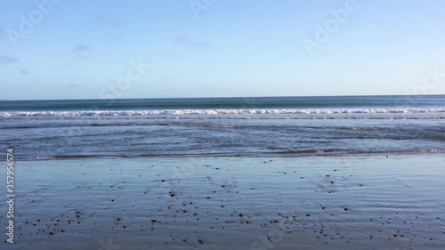 Ocean waves crashing on the shoreline on a sunny day; wet sandy beach in the foreground; Drakes Beach, Point Reyes National Shoreline, California