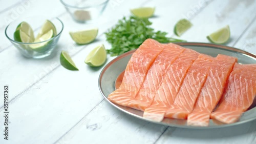 Close-up of slices of fresh raw red salmon.
Raw salmon in a silver plate on the wooden table with lemon and herbs/greens ingredients on the side. Concept of healthy seafood. Salmon 4K.