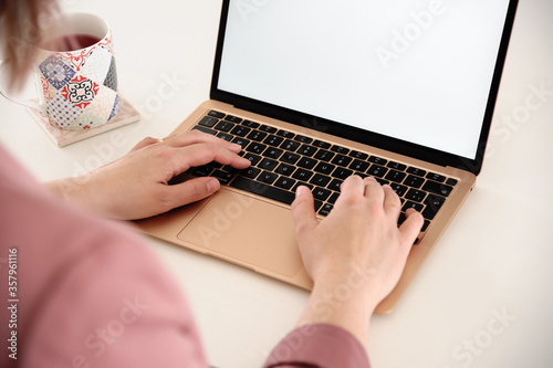 Woman hands using a gold laptop, incredibly thin, light and perfectly portable notebook open with blank white screen on a white wooden table, with a cup of tea infusion.