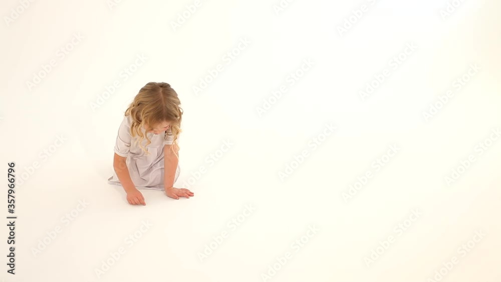 Toddler baby child girl rosy cheeks blond curly hair white dress sitting drawing heart fingers on floor white background Toddler baby child girl rosy cheeks blond curly hair white dress sitting drawing heart fingers on floor white background