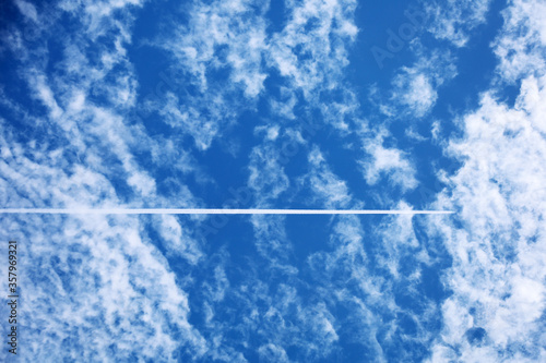 Long trail of airplane flying along the cloudy blue sky