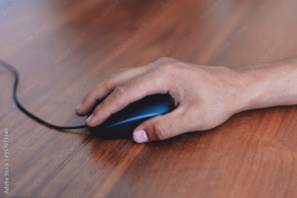A man uses a computer mouse on a wooden table. Side view A man uses a computer mouse on a wooden table. Side view