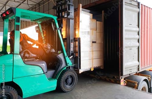 Forklift Tractor Loading Packaging Boxes on Pallets into Shipping Container at Dock Warehouse. Delivery Cargo Trucks Service. Distribution Warehouse Logistics. Shipment Freight Truck Transportation.