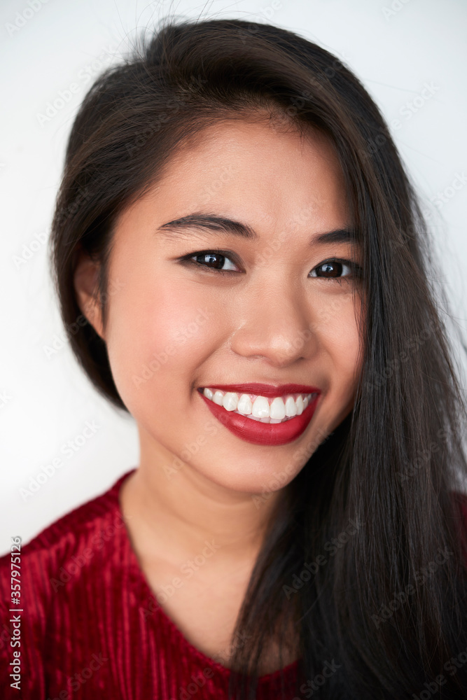 Vertical close-up studio portrait of cheerful attractive young Asian woman with dark-red lips looking at camera smiling, white background Vertical close-up studio portrait of cheerful attractive young Asian woman with dark-red lips looking at camera smiling, white background