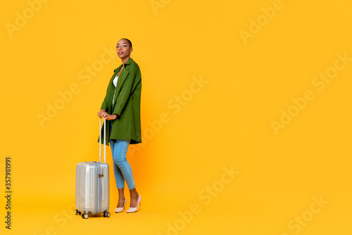 Full body portrait of beautiful fashionable African American woman tourist with baggage isolated on yellow background with copy space