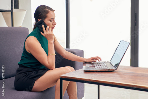 Mujer trabajando en casa, contestando llamada por celular, trabajando desde la sala de su casa.