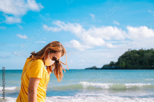 Young asian woman tourist wearing protective face mask travel on the beach in Thailand summer Corona virus travel corona virus spread prevention.