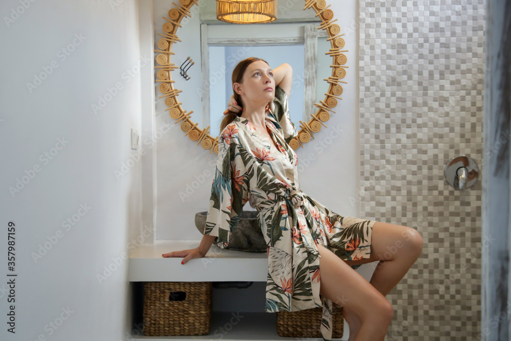 Obraz premium Portrait of beautiful young woman wearing silk in bathrobe in bathroom in front of the mirror