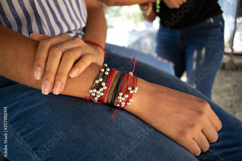 woman's hand with red, green and gold bracelet on jean pants