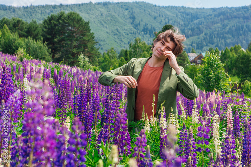 Tall handsome man standing and dancing on lupine flowers field