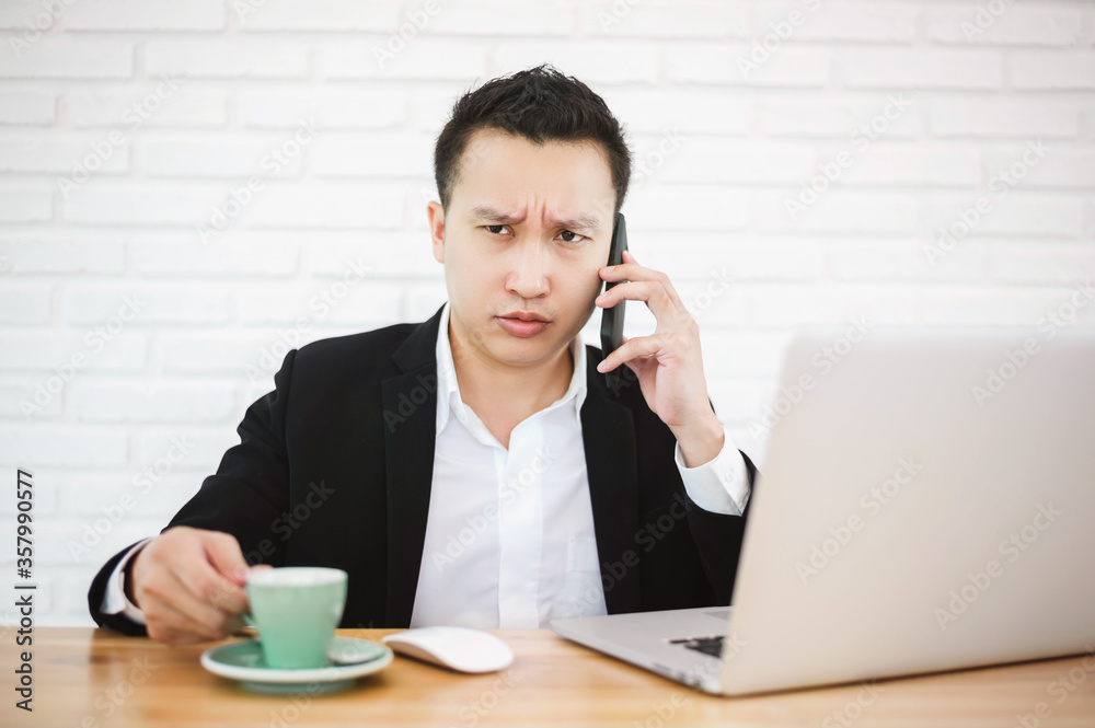 Serious asian businessman working with laptop in the modern office, talking on the phone with his hand still holding a cup of coffee. Serious asian businessman working with laptop in the modern office, talking on the phone with his hand still holding a cup of coffee.