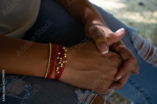 woman's hand with red and gold bracelet on jean pants © Juan