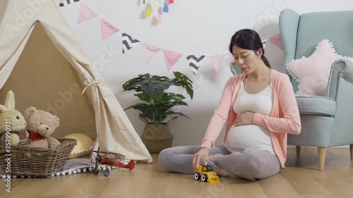 asian mother sitting in game room is trying to bond with her baby during pregnancy by talking to it. taiwanese lady is speaking to her unborn child gently while playing with a toy car