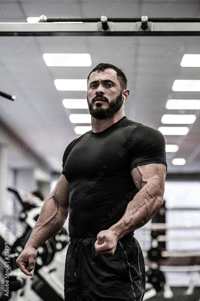 young bearded athlete in black jersey with strong muscle an vein in gym during posing young bearded athlete in black jersey with strong muscle an vein in gym during posing