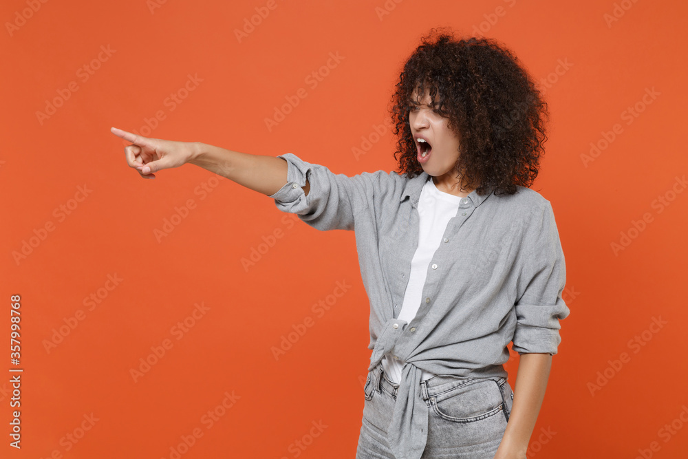 Irritated angry young african american woman girl in gray casual clothes isolated on orange background. People lifestyle concept. Mock up copy space. Pointing index finger aside, swearing screaming. Irritated angry young african american woman girl in gray casual clothes isolated on orange background. People lifestyle concept. Mock up copy space. Pointing index finger aside, swearing screaming.
