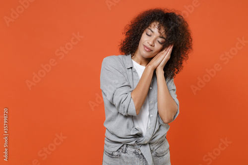 Young african american woman girl in gray casual clothes isolated on orange wall background studio portrait. People emotions lifestyle concept. Mock up copy space. Sleep with folded hands under cheek. © ViDi Studio