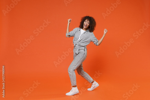 Happy young african american woman girl in gray casual clothes posing isolated on orange background studio portrait. People emotions lifestyle concept. Mock up copy space. Clenching fists like winner.