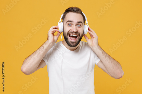 Excited young bearded man guy in white casual t-shirt posing isolated on yellow background studio portrait. People sincere emotions lifestyle concept. Mock up copy space. Listen music with headphones.