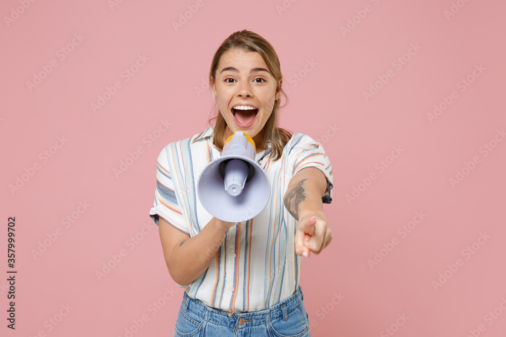 Excited young blonde woman girl in casual striped shirt posing isolated on pastel pink background. People lifestyle concept. Mock up copy space. Scream in megaphone, pointing index finger on camera. Excited young blonde woman girl in casual striped shirt posing isolated on pastel pink background. People lifestyle concept. Mock up copy space. Scream in megaphone, pointing index finger on camera.