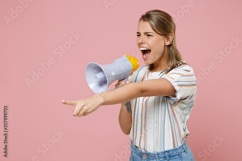 Nervous young blonde woman girl in casual striped shirt posing isolated on pastel pink background. People lifestyle concept. Mock up copy space. Screaming in megaphone, pointing index finger aside.