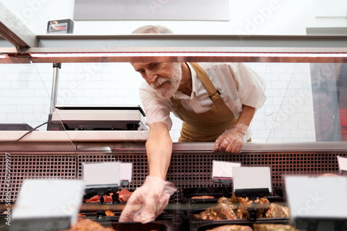Male butcher taking raw meat out of counter.