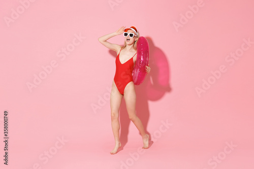 Excited young woman in red one-piece swimsuit cap glasses isolated on pink background. People summer vacation rest concept. Mock up copy space. Hold swim inflatable ring, looking far away distance. © ViDi Studio