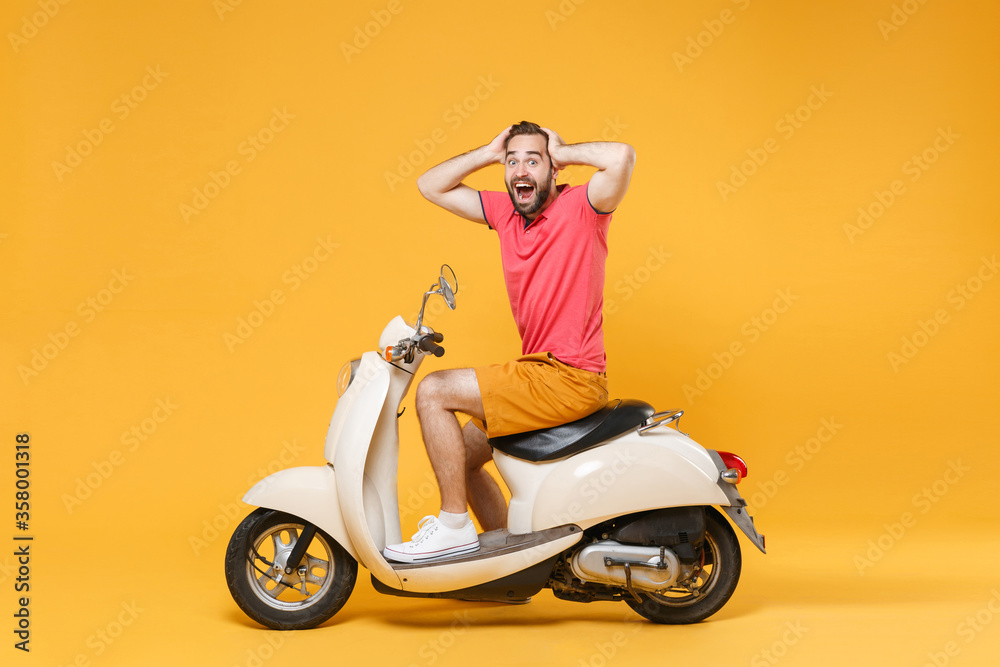 Side view of shocked young bearded man guy in casual summer clothes driving moped isolated on yellow background studio. Driving motorbike transportation concept. Mock up copy space. Put hands on head. Side view of shocked young bearded man guy in casual summer clothes driving moped isolated on yellow background studio. Driving motorbike transportation concept. Mock up copy space. Put hands on head.