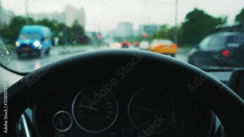 Driving a car in a big city in the rain. POV. 
Selective focus on steering wheel.