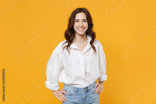 Smiling young brunette business woman in white shirt posing isolated on yellow background studio portrait. Achievement career wealth business concept. Mock up copy space. Standing with arms akimbo.