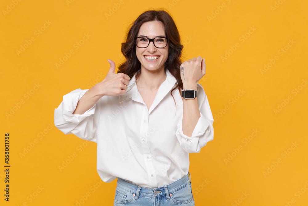 Smiling brunette business woman in white shirt glasses isolated on yellow background. Achievement career wealth business concept. Mock up copy space. Wearing smart watch on hand, showing thumb up. Smiling brunette business woman in white shirt glasses isolated on yellow background. Achievement career wealth business concept. Mock up copy space. Wearing smart watch on hand, showing thumb up.