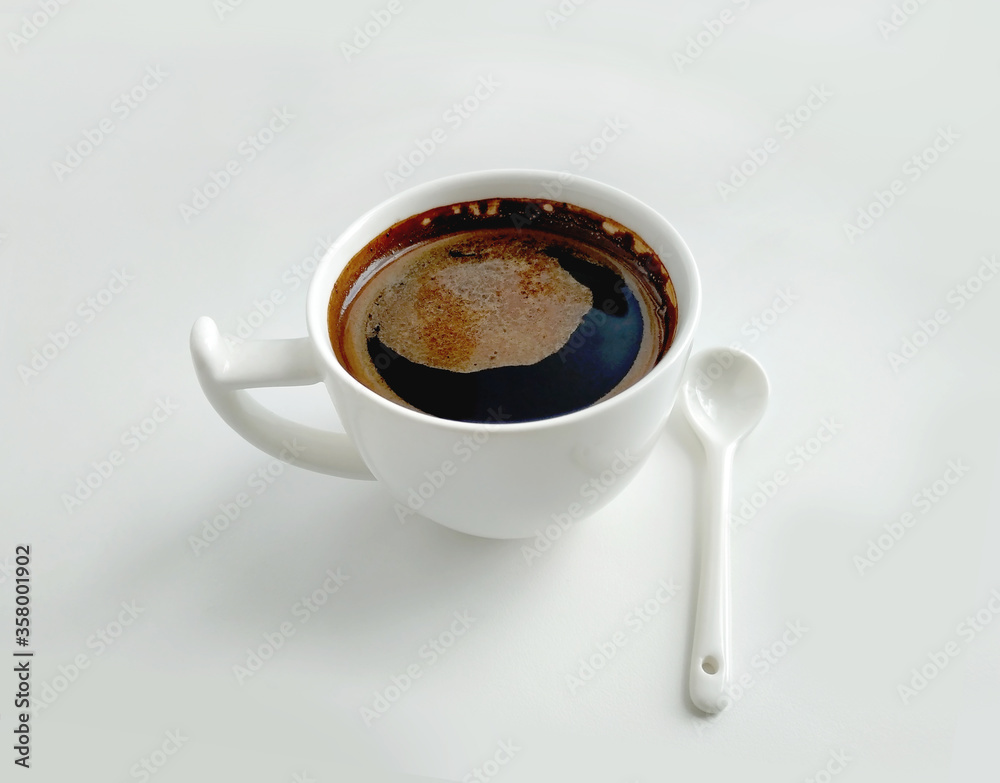 White cup of coffee and white ceramic spoon on a white background White cup of coffee and white ceramic spoon on a white background