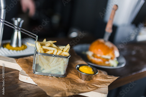 Billede på lærred French fries in basket and cheese sauce on wooden cutting board on table