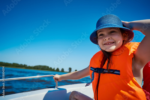 little girl in a swimming vest sits in a motorboat 