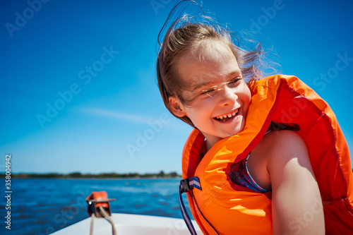 Obraz na płótnie little girl in a swimming vest sits in a motorboat w salonie