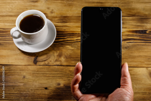 Hand with modern smartphone and cup of coffee on a rustic wooden table