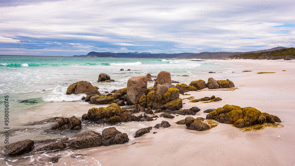 Rocks on the beach, Tasmania, Australia. Light blue ocean and white sand beach with rocks and moss. Remote beach landscape.