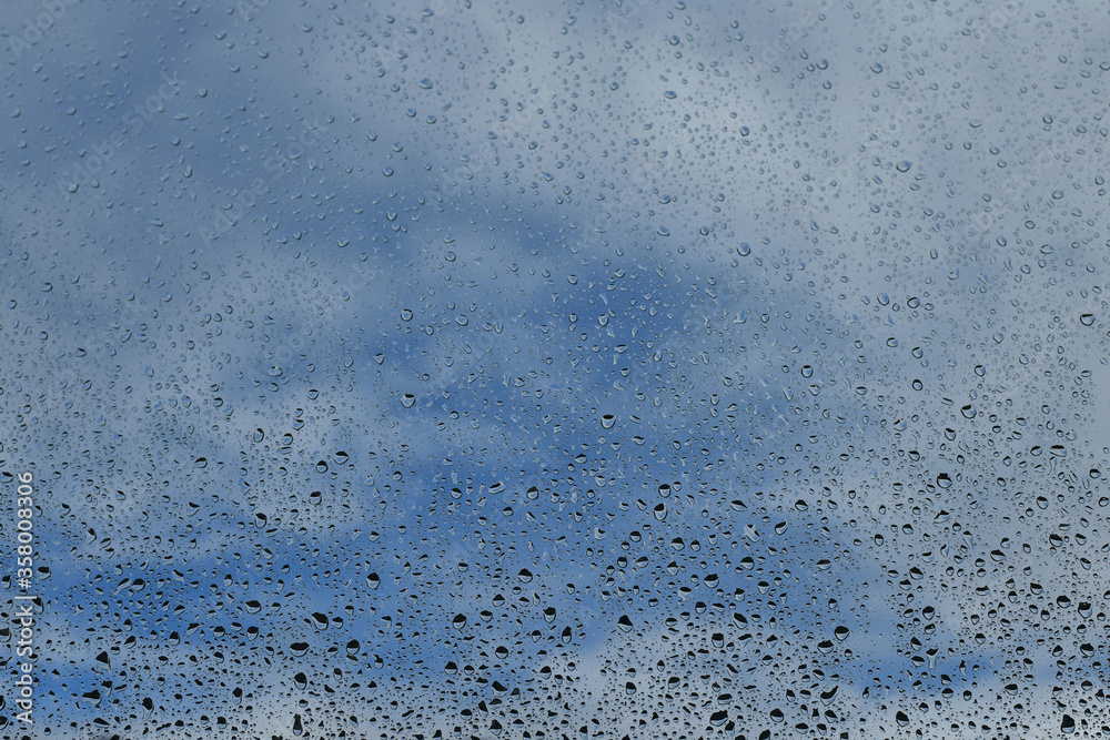 Raindrops on window with cloudy blue sky background