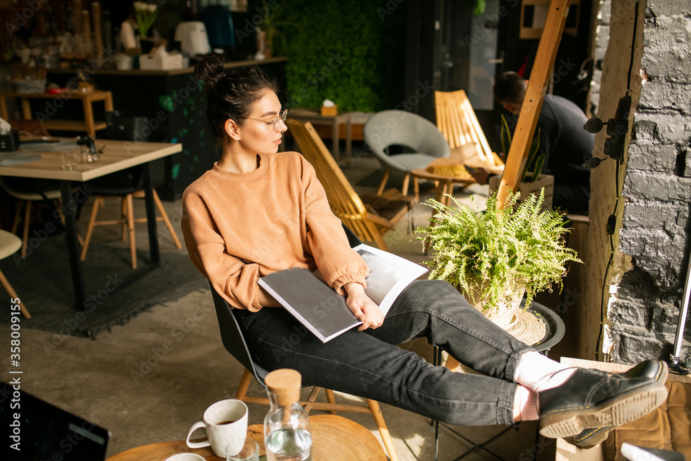 young stylish girl girl drinks coffee. Girl blogger with a cup of coffee in cafe with magazine young stylish girl girl drinks coffee. Girl blogger with a cup of coffee in cafe with magazine