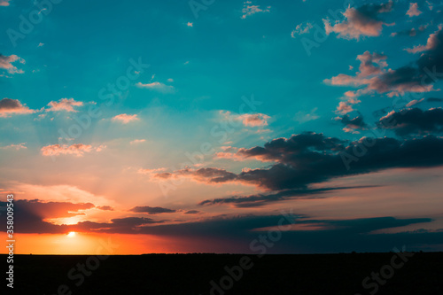 Sunset sunrise over field or meadow. Bright dramatic sky and dark ground. Countryside landscape under scenic colorful sky at sunset dawn sunrise.