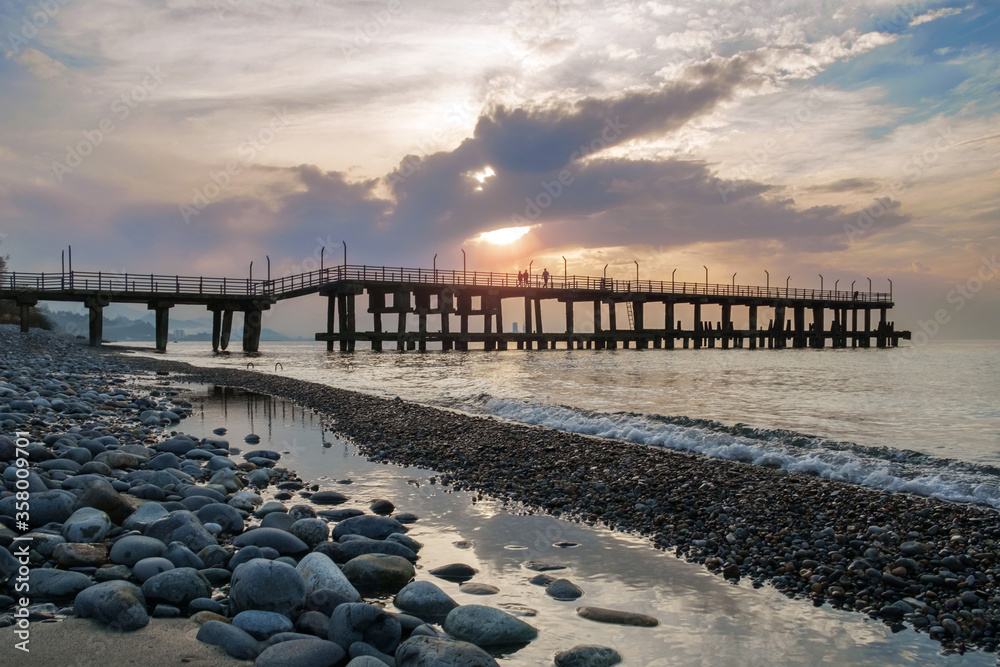 Pier at the rocky beach with puddles and sunset sky background