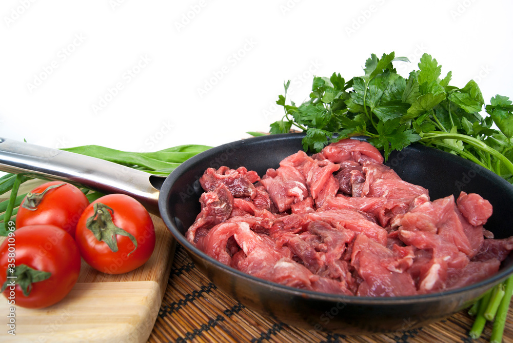 Fresh raw chopped beef in a pan with tomato and herbs on the kitchen table Fresh raw chopped beef in a pan with tomato and herbs on the kitchen table