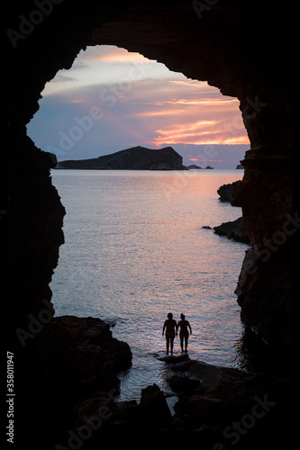 Silhouette of two women in a cove in Ibiza with the sunset in the background. Friendship and human relations